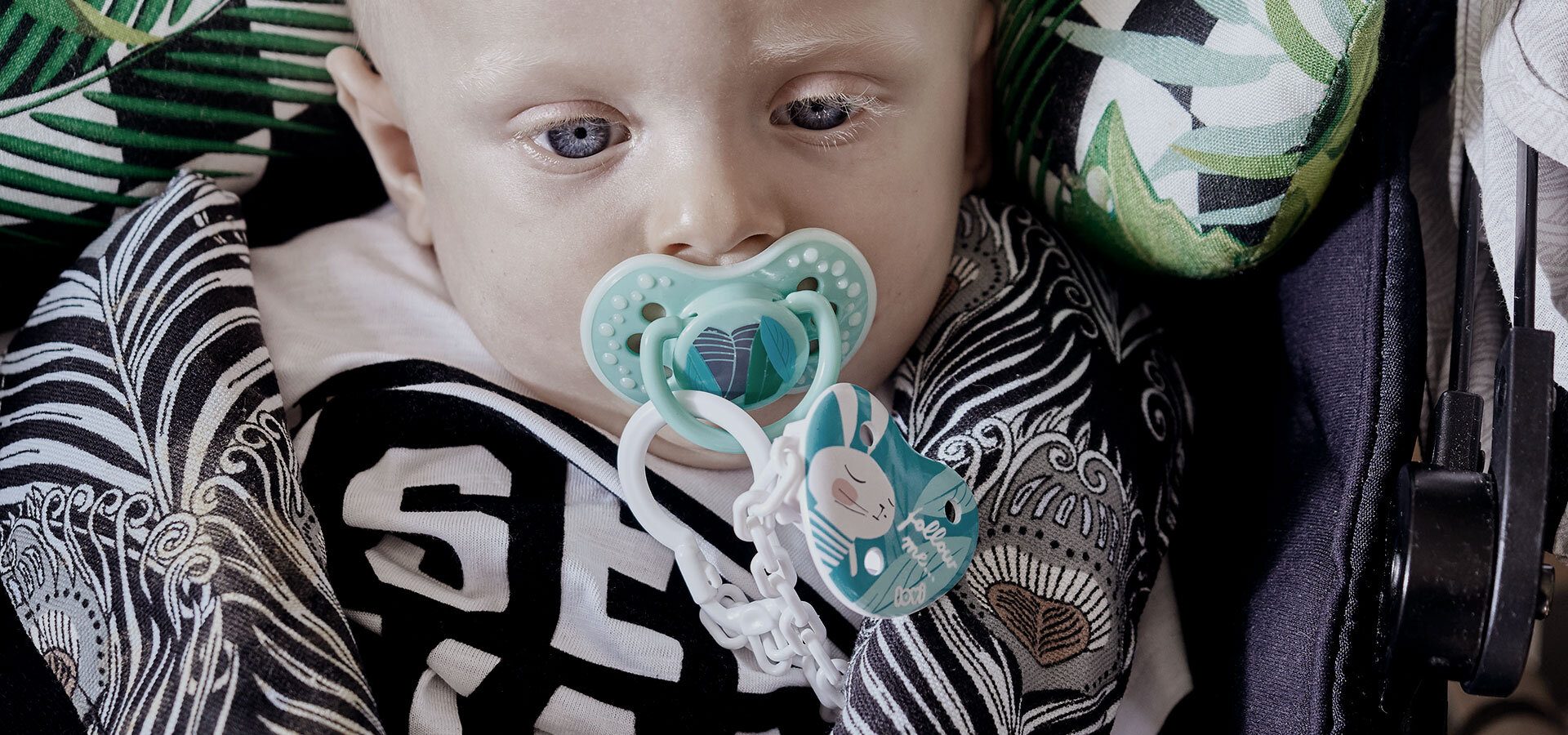 A baby boy sitting in a car seat with a lovi soother and a soother holder from the follow the rabbit collection