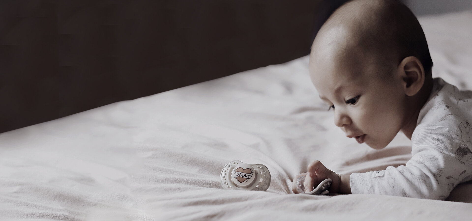 Маленький мальчик лежит на кровати и держит соску-пустышку